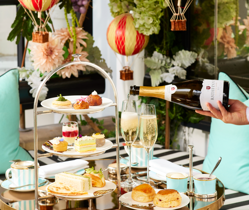 Afternoon tea set out on a table, with a waiting pouring champagne, and decorative miniature hot air balloons above and in the background