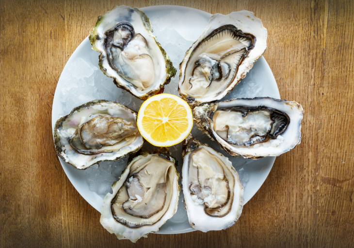 A plate with six oysters laid out in a circle, and half a lemon in the centre