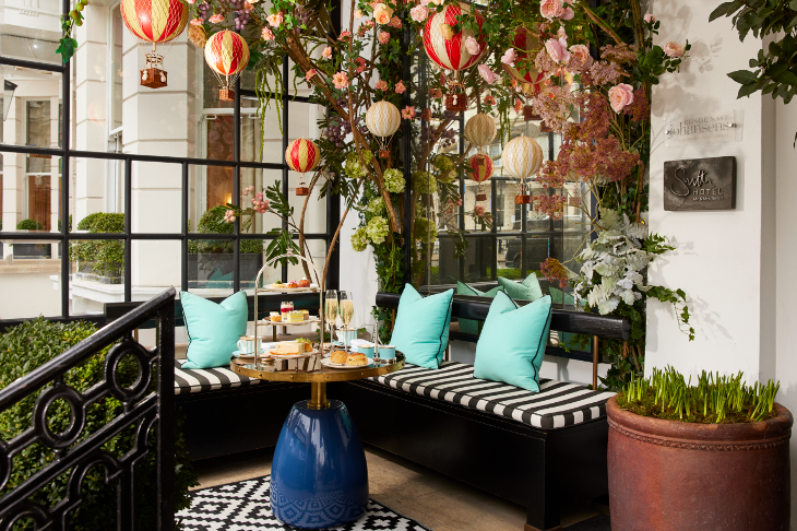 A table in the corner of a restaurant, with hot air balloons suspended above and fake flowers behind it. It's set up for afternooon tea with a three-tiered stand and glasses of champagne