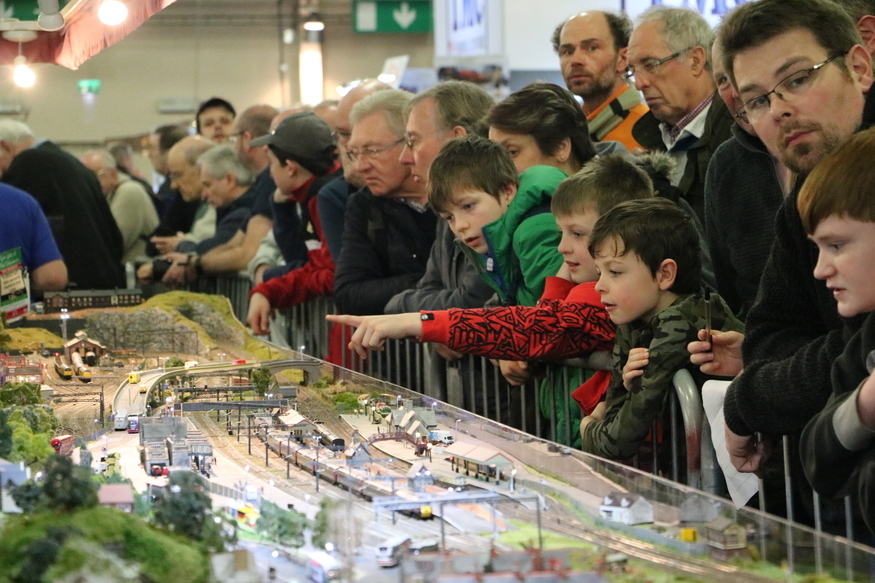 kids and adults watch and point at miniature trains