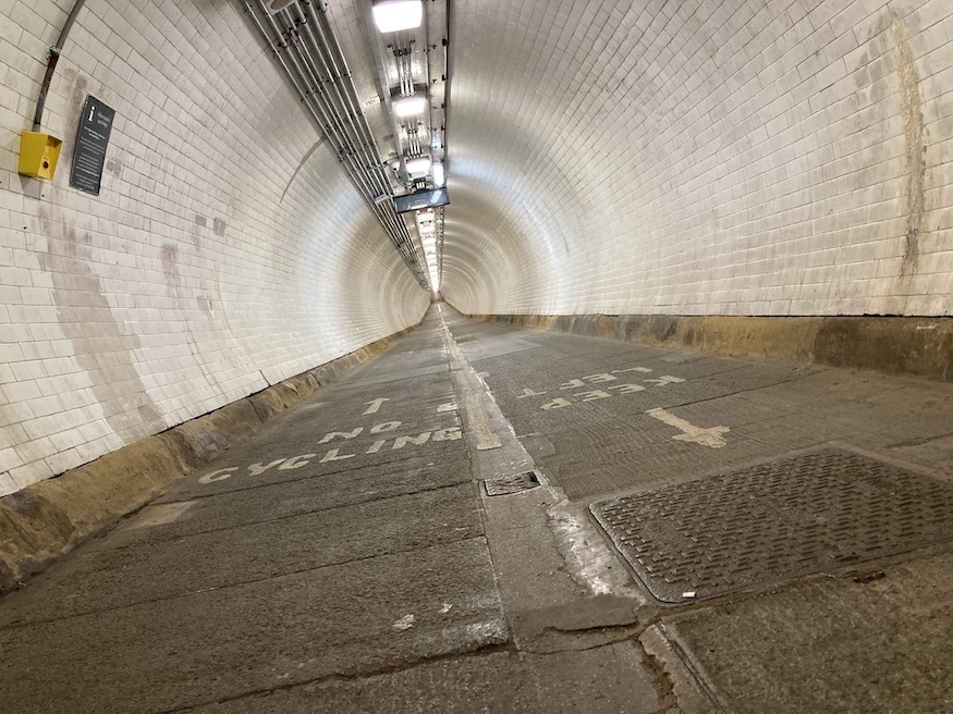 A view along the Woolwich foot tunnel taken at floor level. It is a white tiled tunnel with left and right marked lanes