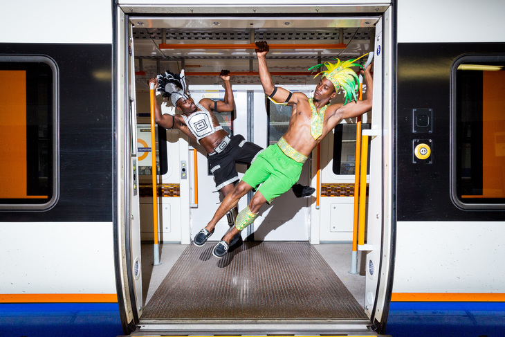 two men in carnival outfits hanging from the ceiling of an overground train