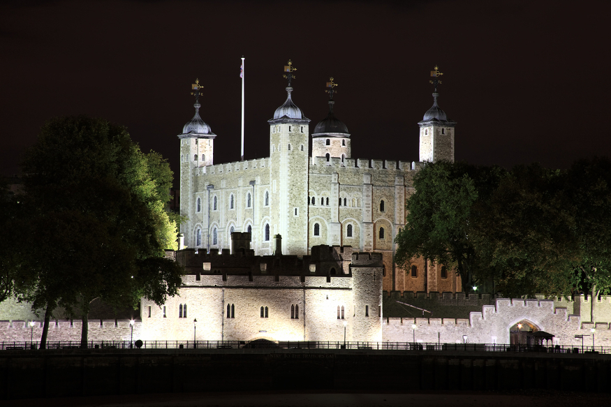 The Tower of London illuminated against a black sky at night.
