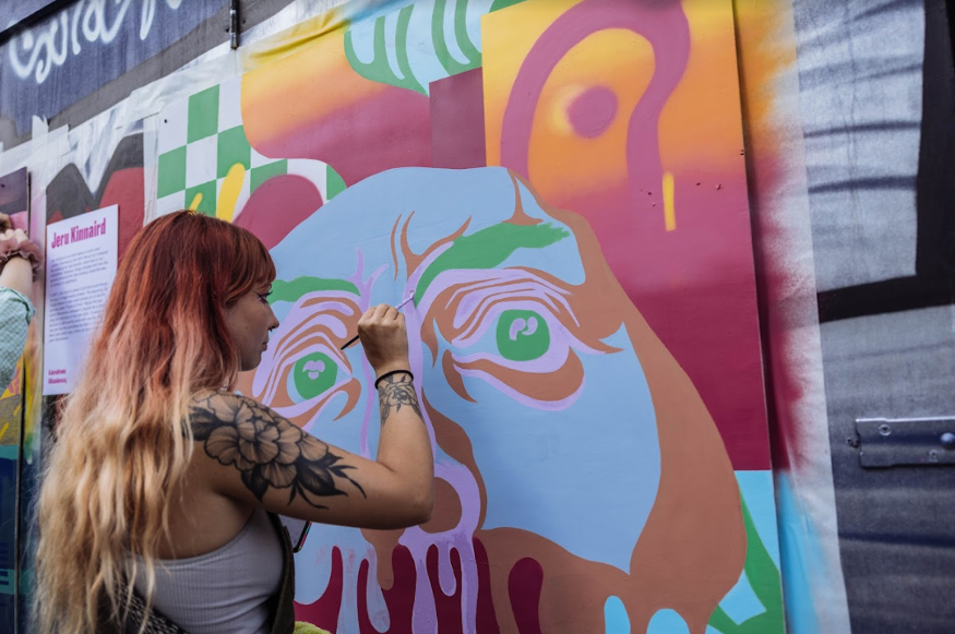 A woman painting a colourful mural onto a wall.