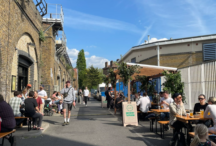 People sitting at picnic tables drinking, alongside the railway arches in Deptford.