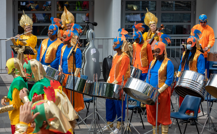 Musicians dressed in blue and orange costumes performing on the steel pan drums.