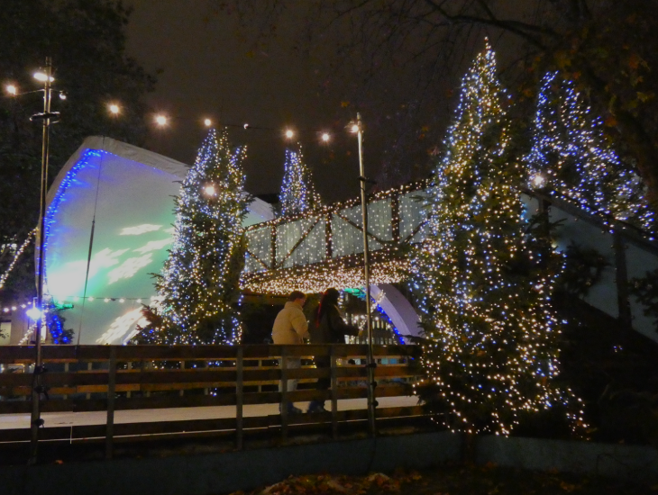 People skating beneath a pedestrian footbridge covered in twinkling lights