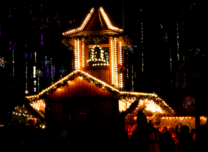 A wooden chalet with a bell tower, outlined with Christmas lights