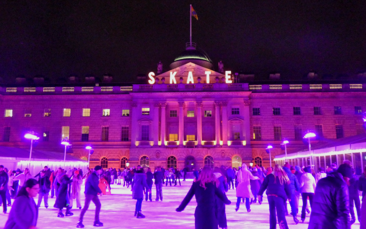 People skating in front of Somerset House, with the facade illuminated in pink