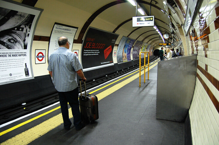 A man waits on a tube platform with a suitcase