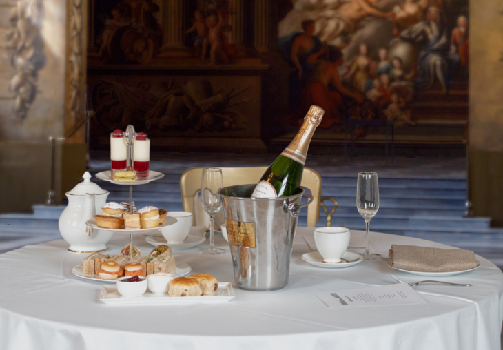 Afternoon tea alongside a champagne ice bucket, with the Painted Hall artworks in the background
